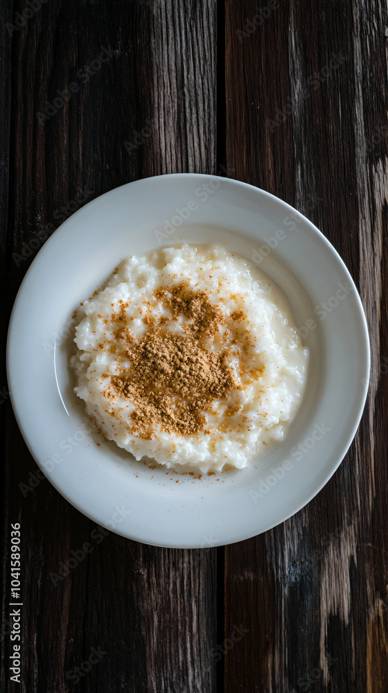 White rice pudding sprinkled with cinnamon powder, served on a white plate over a rustic wooden table White rice pudding sprinkled with cinnamon powder, served on a white plate over a rustic wooden table