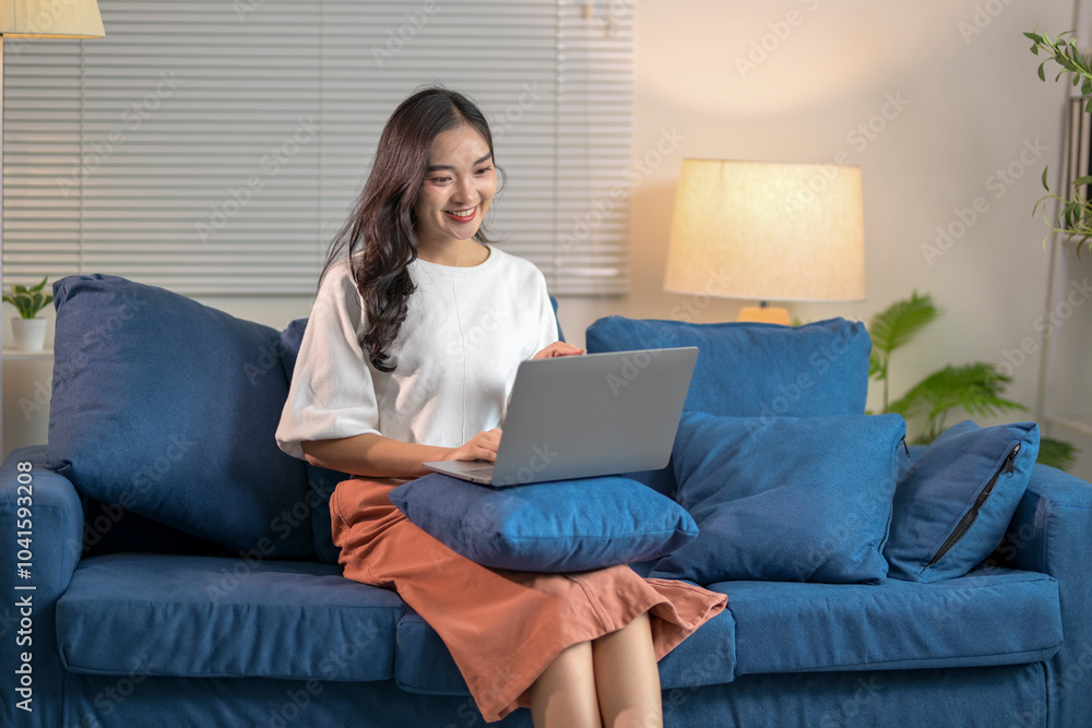 Young asian woman working from home using laptop sitting on sofa in living room Young asian woman working from home using laptop sitting on sofa in living room