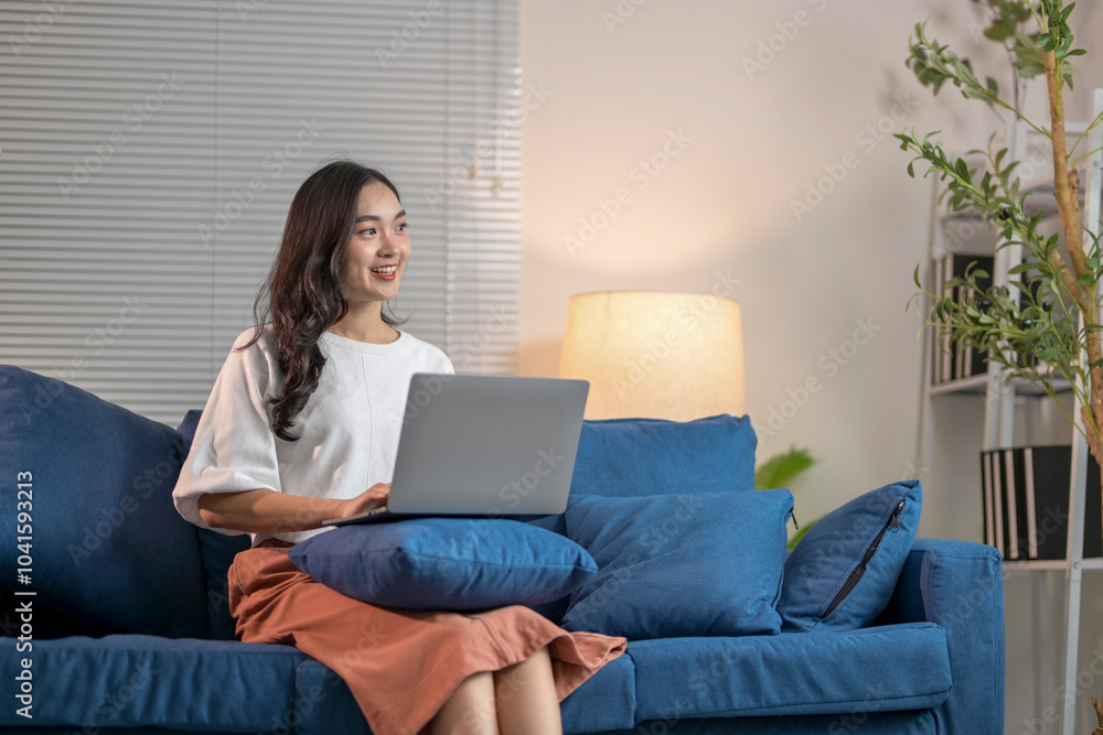 Young woman sitting on sofa using laptop and smiling at home Young woman sitting on sofa using laptop and smiling at home