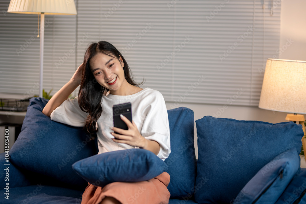 Young woman relaxing on sofa using smartphone at night Young woman relaxing on sofa using smartphone at night