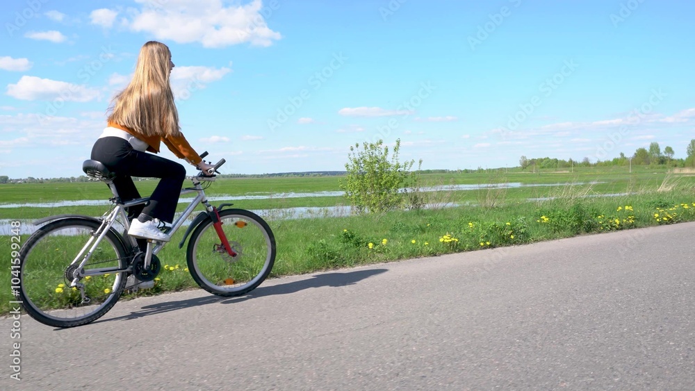 A young blonde girl rides a bicycle past beautiful fields and rivers. A young blonde girl rides a bicycle past beautiful fields and rivers.