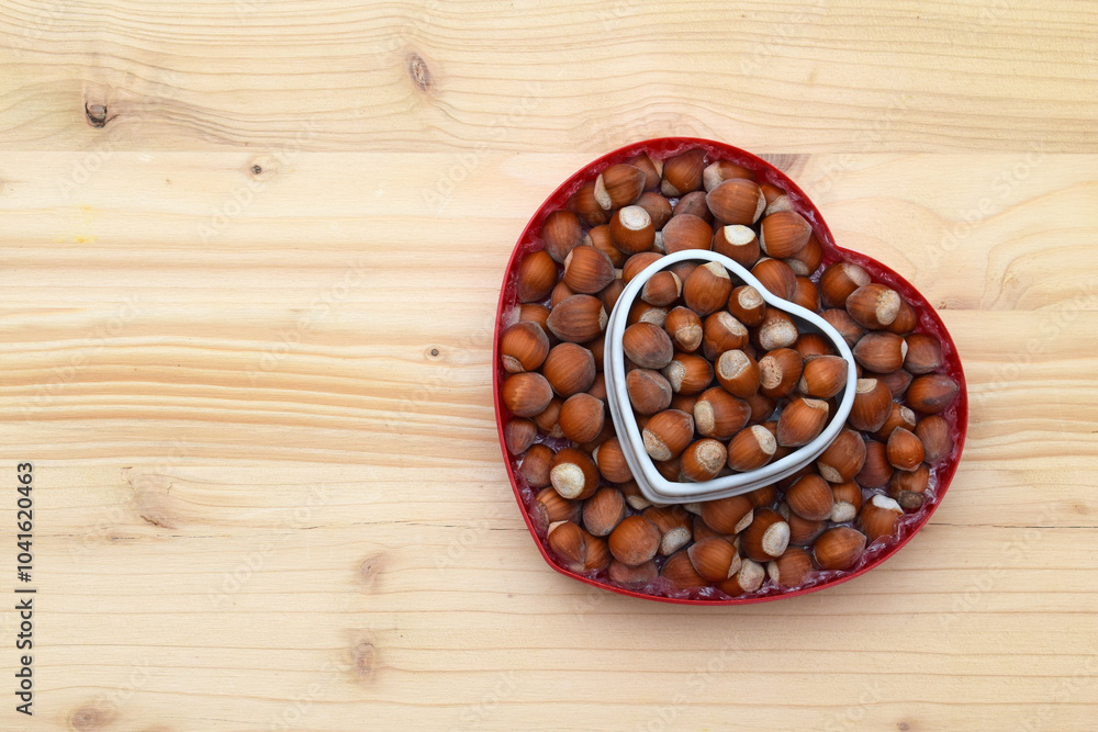 Obraz premium Hazelnuts in shell on heart shaped bowls, wooden background, copy space for text
