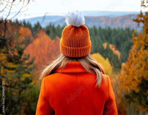 Woman wearing an orange coat and orange woolly hat looking at a view of an autumn forest