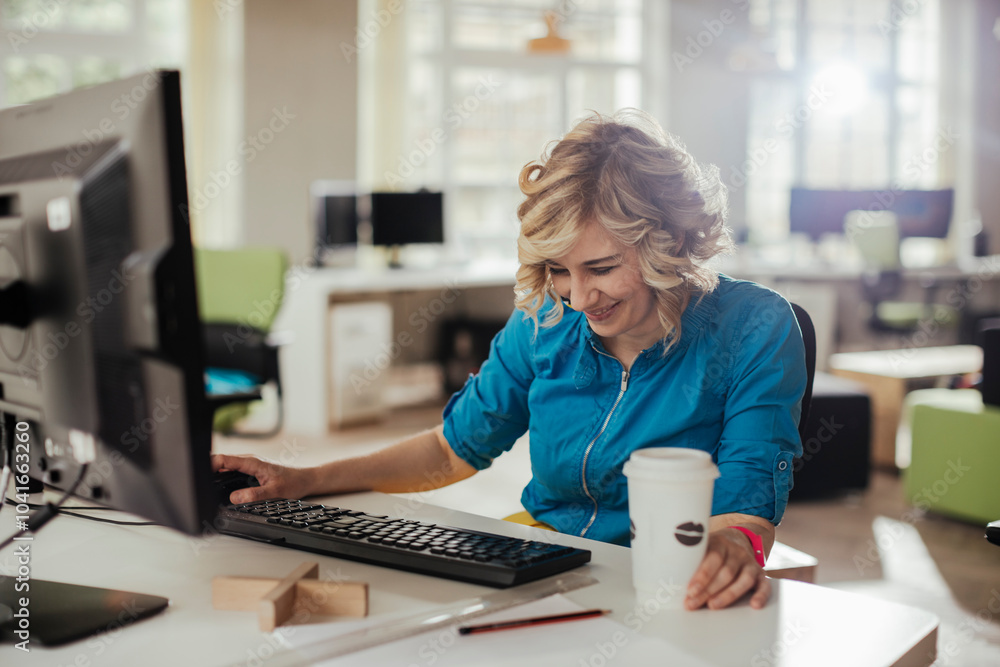 Young woman having coffee while using a computer and working in a startup company office Young woman having coffee while using a computer and working in a startup company office