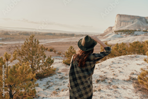 Woman in plaid shirt and hat gazes at majestic mountain view from hilltop perch