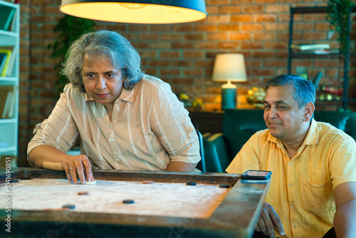 Indian couple in their fifties playing carrom indoors, smiling, enjoying a fun and relaxed moment photo