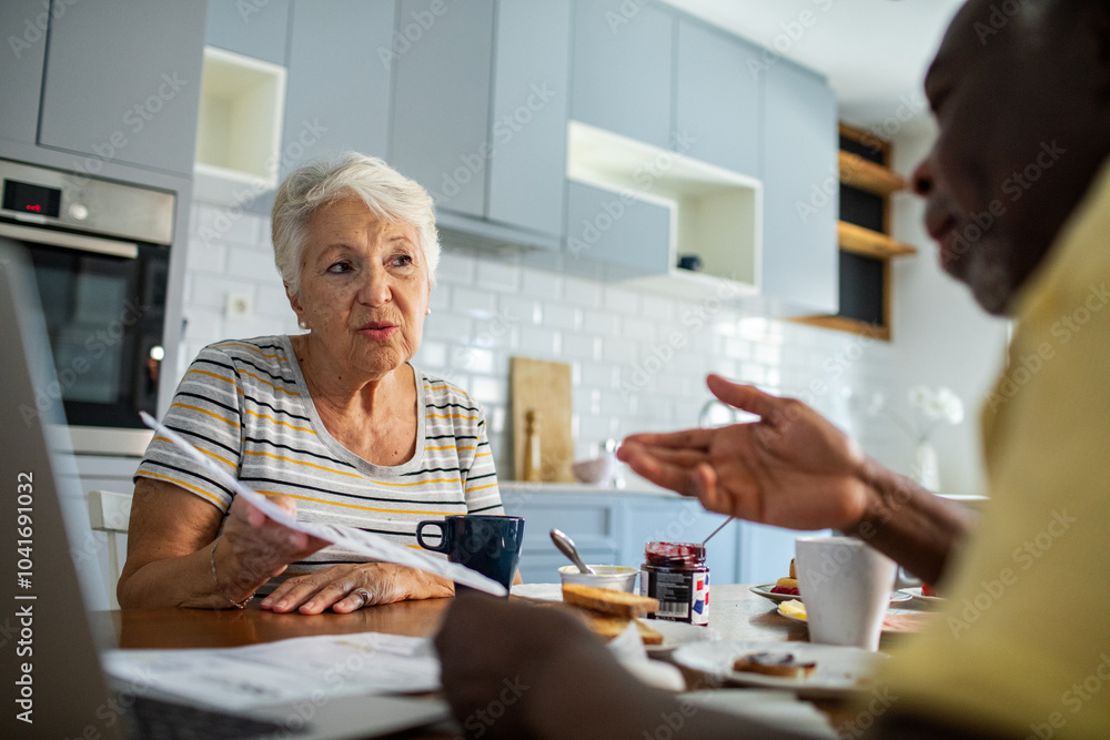 Senior couple discussing bills at kitchen table Senior couple discussing bills at kitchen table