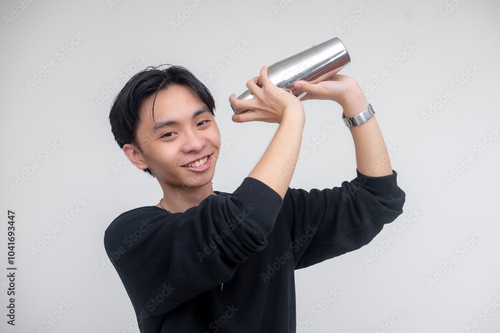 A casual young asian bartender smiling while mixing a drink with a cobbler shocker. Isolated on a white background. A casual young asian bartender smiling while mixing a drink with a cobbler shocker. Isolated on a white background.