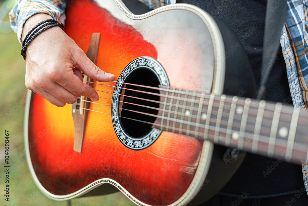 Male hands with an acoustic guitar against a background of a country landscape.