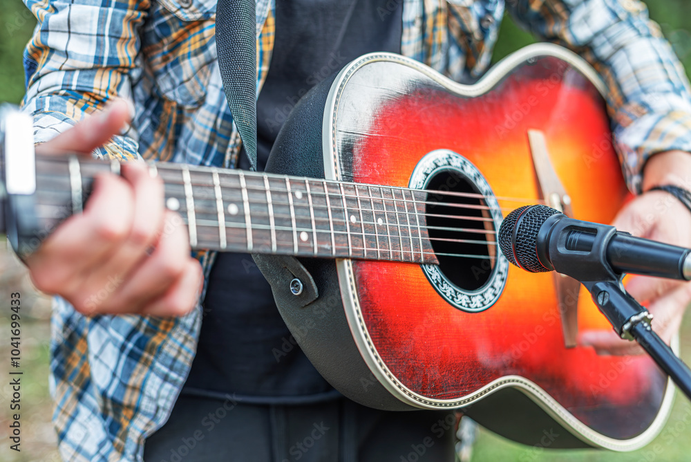 Male hands with an acoustic guitar against a background of a country landscape.
