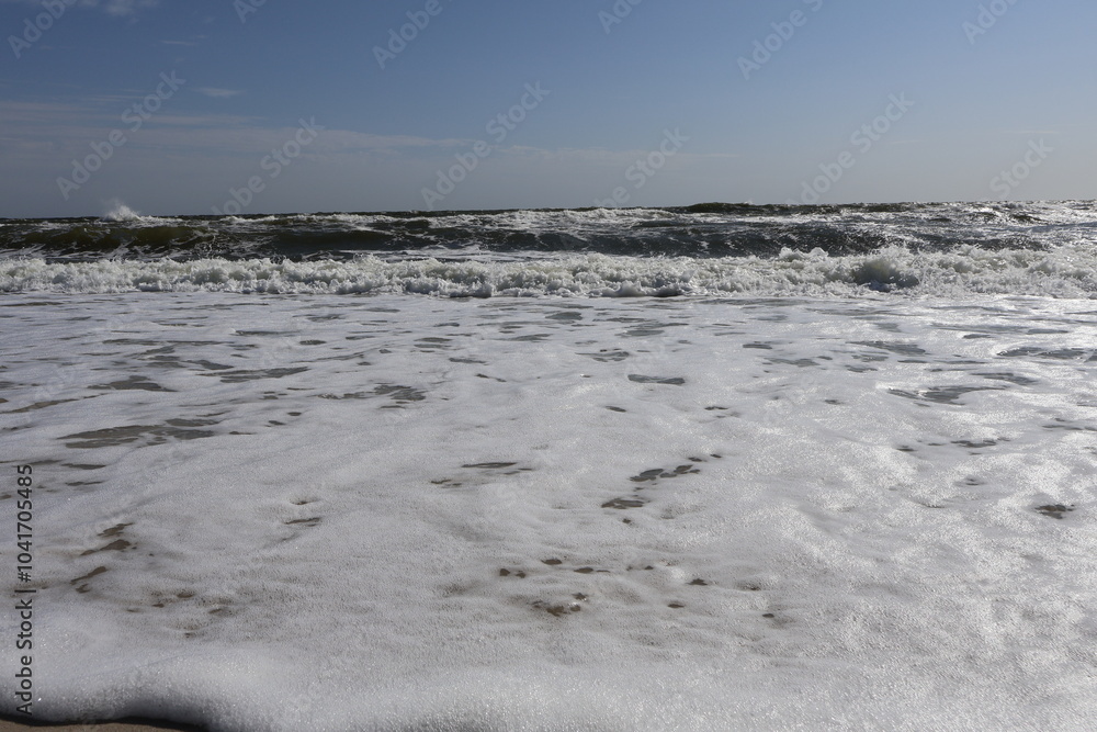Close-up View of White Ocean Foam Covering Sandy Beach with Rolling Waves in Background Close-up View of White Ocean Foam Covering Sandy Beach with Rolling Waves in Background