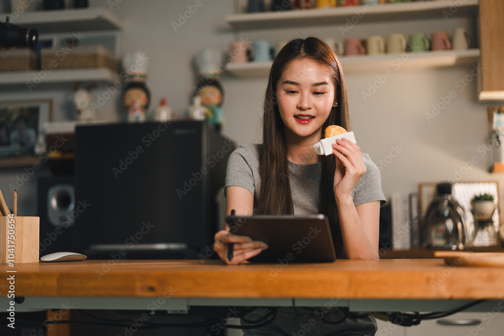 Enjoying snack while using tablet, young woman sits at wooden table in cozy kitchen. scene captures moment of relaxation and engagement with technology Enjoying snack while using tablet, young woman sits at wooden table in cozy kitchen. scene captures moment of relaxation and engagement with technology