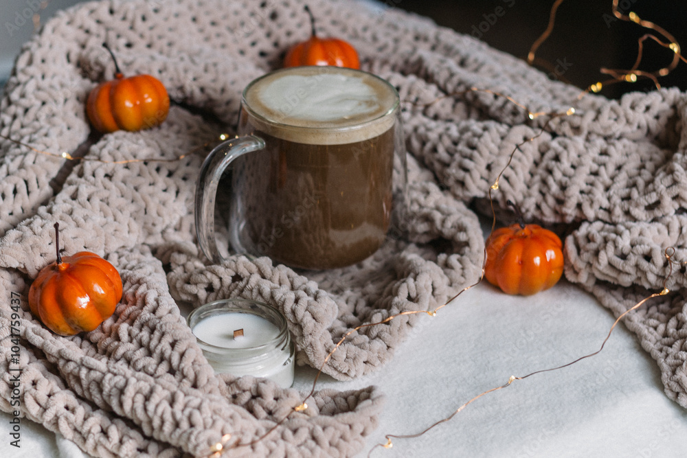 Autumn cozy still life. Black coffee with milk in a glass mug on the table in a warm beige knitted plaid and orange pumpkins. A place for the text. Thanksgiving and Halloween