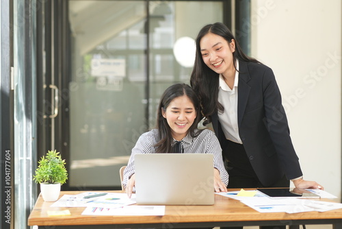 Happy Asian business people working together using laptop and tablet in office.