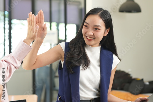 Two female managers happily shake hands in an office meeting.