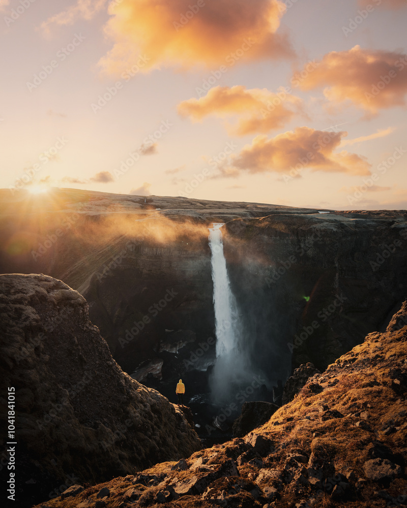 Stunning view of the Haifoss Waterfall with a tourist wearing a yellow jacket during a breathtaking sunset. Haifoss Waterfall is the third highest waterfall in Iceland.