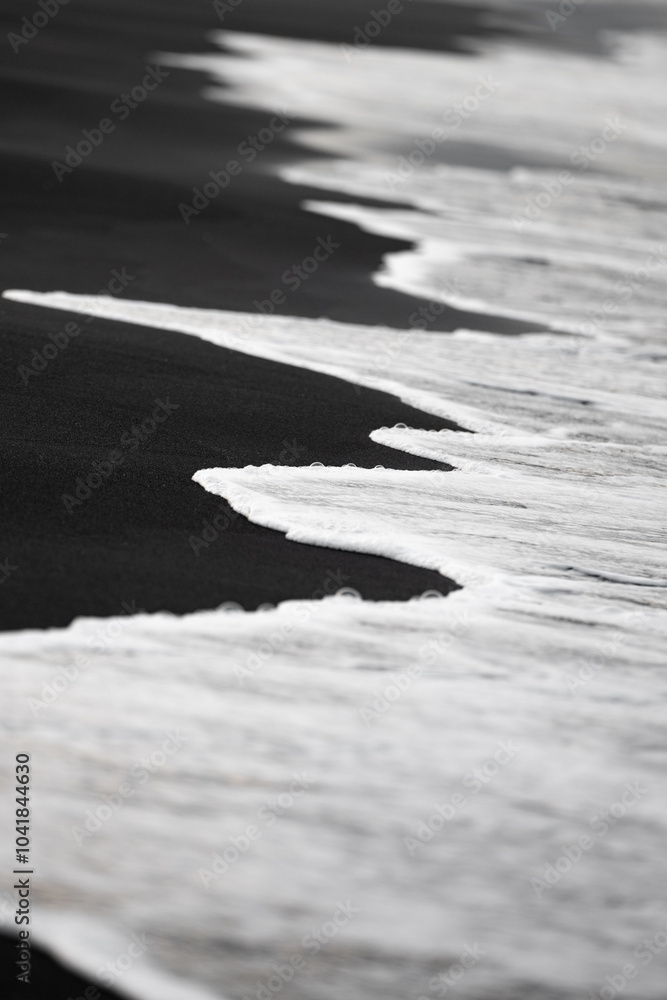 Close-up view of some waves crashing on a black sand beach. Natural background, wallpaper. Iceland.