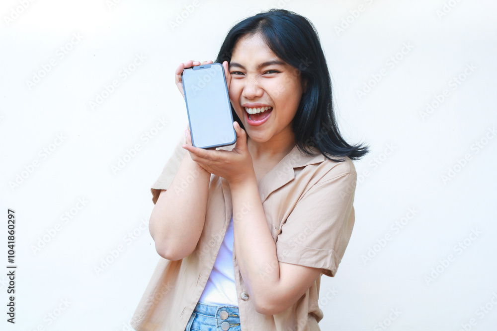 happy asian woman holding smartphone celebrate victory with raised fist wearing casual brown clothes isolated on white background happy asian woman holding smartphone celebrate victory with raised fist wearing casual brown clothes isolated on white background