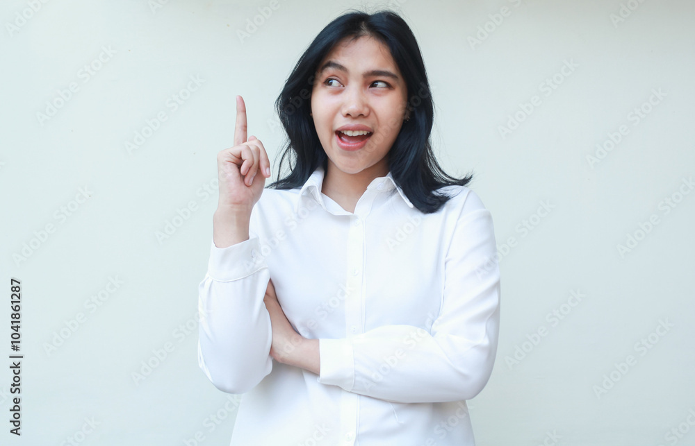 image of carefree asian young business woman pointing up looking above with arms folded thinking something with dreamy face expression wearing white formal suit shirt isolated on white background image of carefree asian young business woman pointing up looking above with arms folded thinking something with dreamy face expression wearing white formal suit shirt isolated on white background