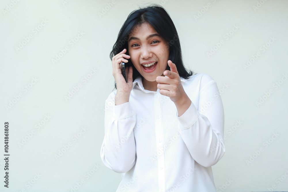 image of playful asian young saleswoman speaking on smartphone pointing finger forwards excited looking at camera show confident smile open mouth wearing white formal shirt, its you gesture, standing image of playful asian young saleswoman speaking on smartphone pointing finger forwards excited looking at camera show confident smile open mouth wearing white formal shirt, its you gesture, standing