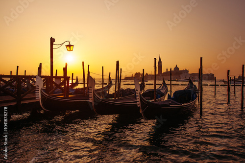 Sunset over the Venetian Lagoon with moored gondolas creating a picturesque view as warm hues illuminate the water; a tranquil moment in Venice capturing the essence of this iconic city. Italy