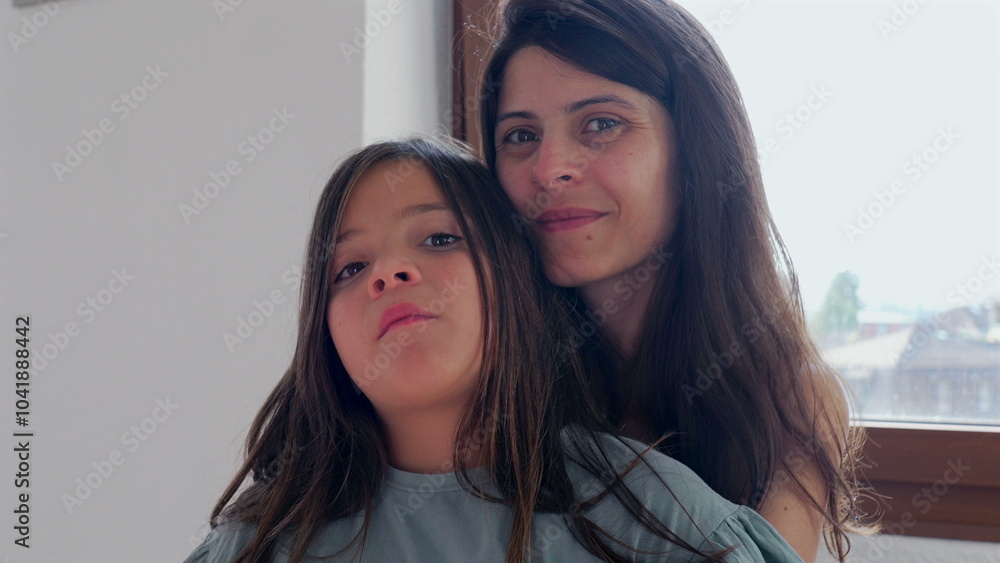 Mother and little girl sitting together by the window, sharing a warm embrace. girl rests comfortably against her mother, creating a tender and loving family moment in a cozy home Mother and little girl sitting together by the window, sharing a warm embrace. girl rests comfortably against her mother, creating a tender and loving family moment in a cozy home
