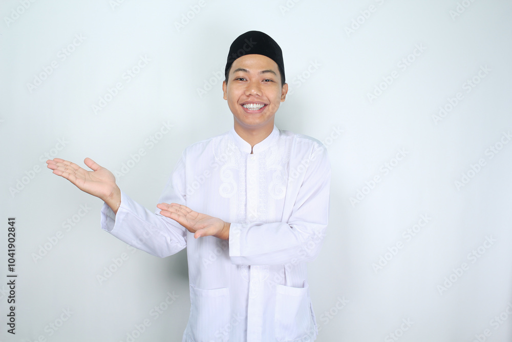 attractive muslim asian man presenting hand to the right side with smiling face isolated on white background, looking at camera attractive muslim asian man presenting hand to the right side with smiling face isolated on white background, looking at camera
