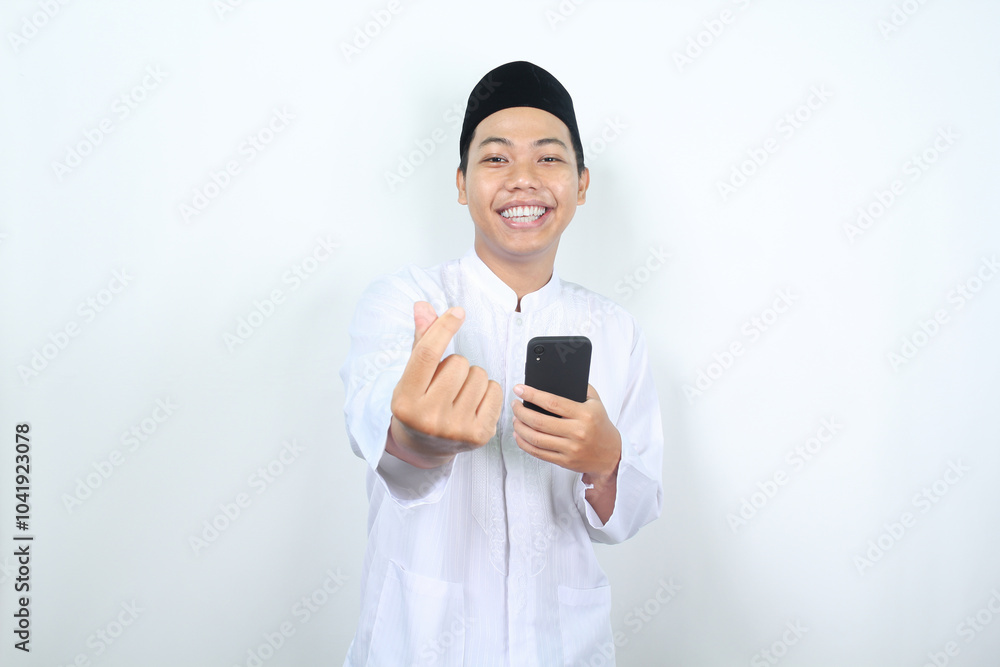 smiling asian muslim man showing korean love signs with holding mobile phone isolated smiling asian muslim man showing korean love signs with holding mobile phone isolated