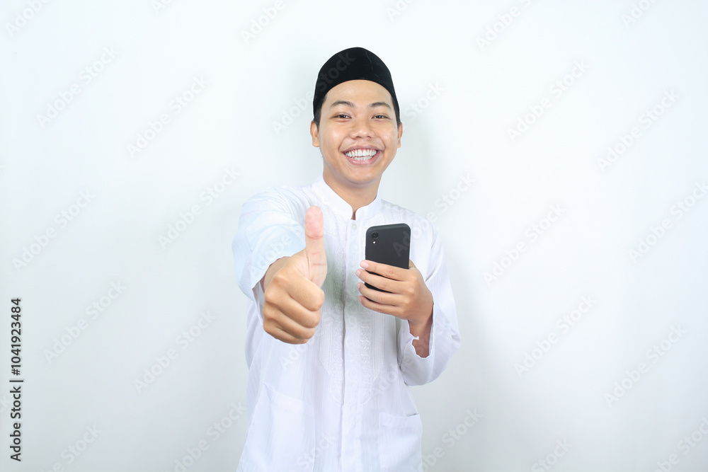 smiling asian muslim man showing thumbs up with holding phone isolated smiling asian muslim man showing thumbs up with holding phone isolated