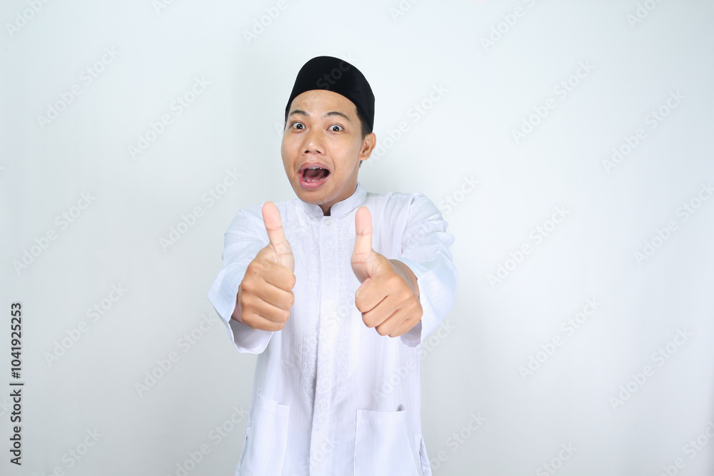 funny asian muslim man giving thumbs up with surprised expression isolated on white background funny asian muslim man giving thumbs up with surprised expression isolated on white background