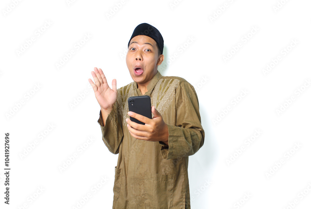 shocked asian muslim man raising hand with holding mobile phone isolated on white background shocked asian muslim man raising hand with holding mobile phone isolated on white background