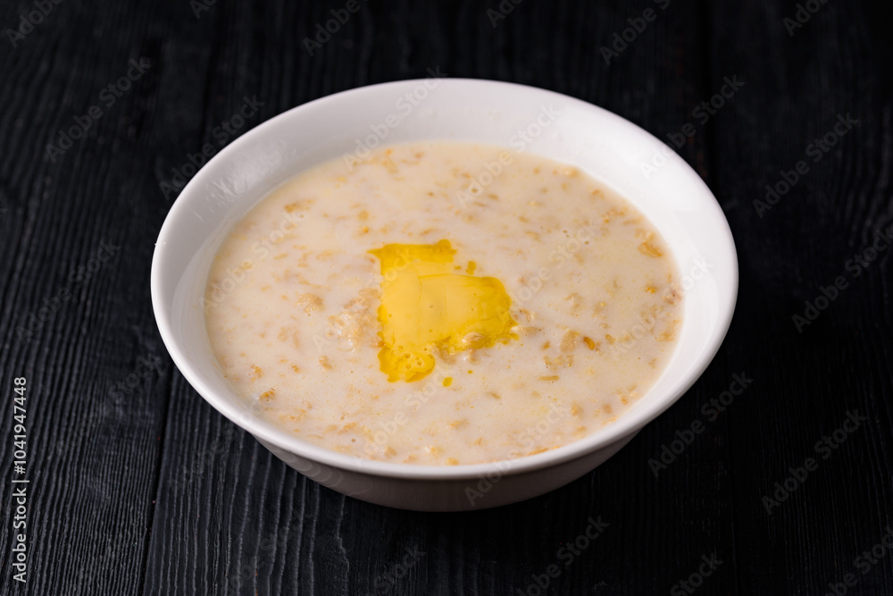 oatmeal porridge with milk and butter. on a black wooden background oatmeal porridge with milk and butter. on a black wooden background
