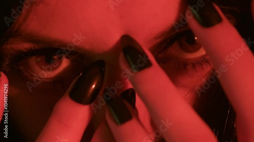 Close-up of a dark-haired witch with intense makeup, scratching her face with black nails in warm candlelight. The video focuses on her eyes, face, and hands in a spooky atmosphere