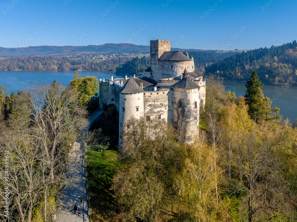 Poland. Medieval castle in Niedzica, dating to 14th century (upper castle) in autumn in October. Trees in beautiful fall colors. Sunrise light. Artificial Czorsztyn lake on Dunajec river. Aerial view