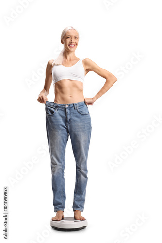 Happy young woman standing on a weight scale in a big pair of jeans