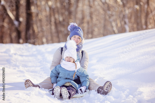 Mother with little daughter slide down from snow slope together sitting in one slide. Winter activities concept image. Happy family time