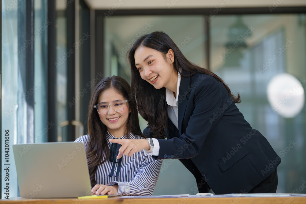 Two young Asian businesswomen discussed investment project work and planning strategy. Business people talk together on laptop computers at the office. Two young Asian businesswomen discussed investment project work and planning strategy. Business people talk together on laptop computers at the office.