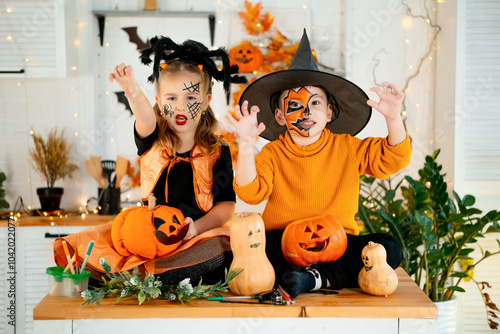 Halloween, two baby boy and girl in festive costumes and makeup are preparing for Halloween at home in the kitchen by coloring and carving pumpkins and scaring everyone photo