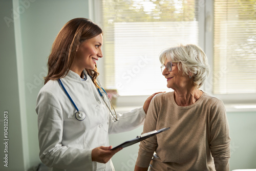 Happy female nurse talking to her senior patient  at doctor's office.