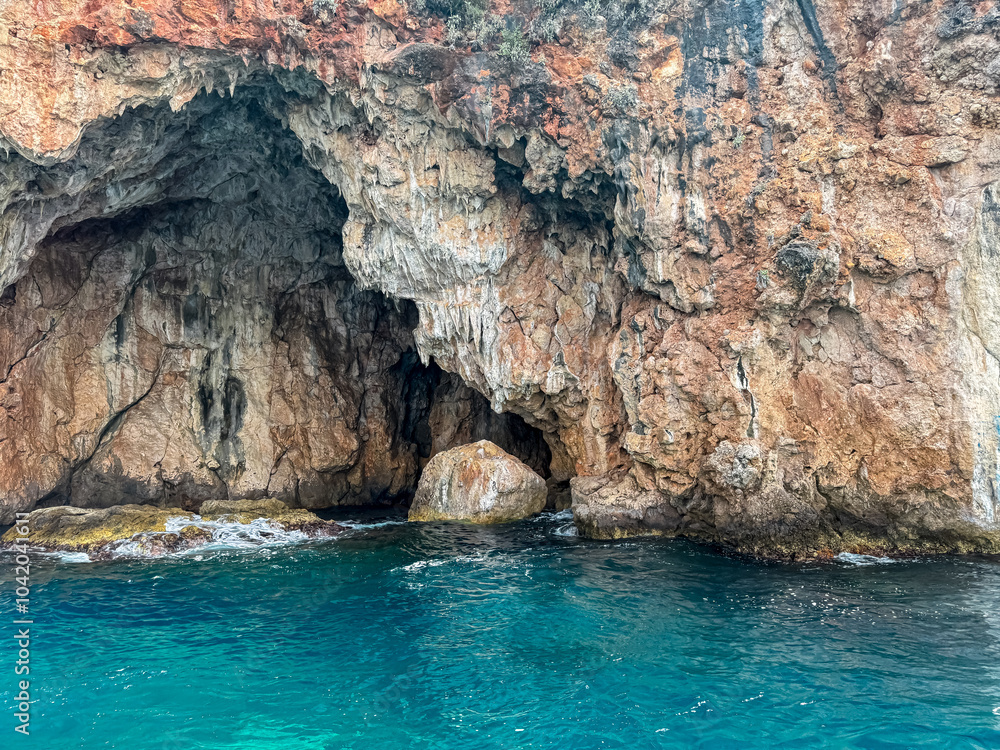 Boat trip with scenic view of large sea cave called Monastery caves near Himare, Vlore, Albania. Dramatic coastal landscape of Albanian Riviera with natural archway. Sightseeing on Mediterranean sea Boat trip with scenic view of large sea cave called Monastery caves near Himare, Vlore, Albania. Dramatic coastal landscape of Albanian Riviera with natural archway. Sightseeing on Mediterranean sea