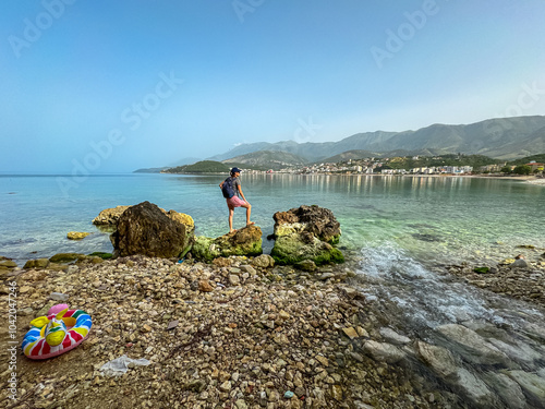 Woman on rock with panoramic view of coastline of tourist town Himare, Vlore, Albania. Sand beach Potami with scenic vistas of majestic Ceraunian mountain range. Summer vacation at Mediterranean sea photo