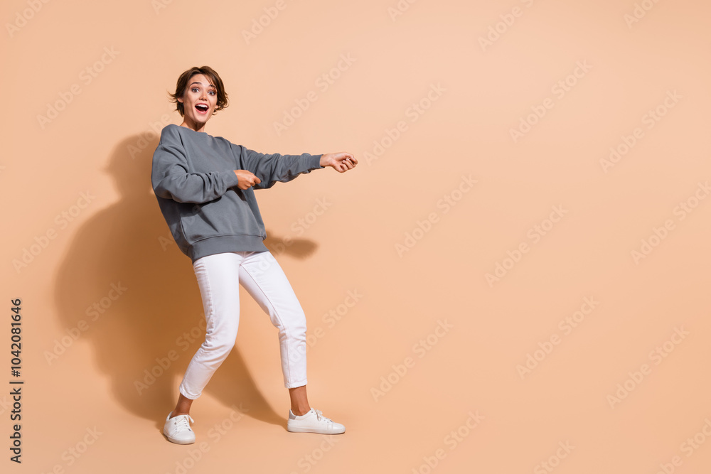 Full size photo of ecstatic overjoyed woman dressed grey pullover pull product from empty space isolated on pastel color background Full size photo of ecstatic overjoyed woman dressed grey pullover pull product from empty space isolated on pastel color background