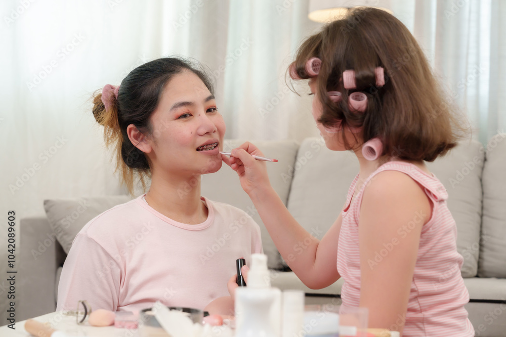 Young girl playfully applying lipstick on mother’s lips during an intimate makeup session. mother smiles warmly, enjoying the affectionate and joyful moment with her daughter in living room setting. Young girl playfully applying lipstick on mother’s lips during an intimate makeup session. mother smiles warmly, enjoying the affectionate and joyful moment with her daughter in living room setting.