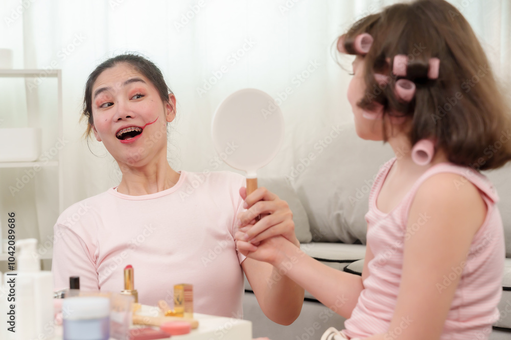 Mother smiling in surprise while holding mirror, reacting to playful makeup done by young daughter. Fun and joyful family moment highlighting the bond between mother and daughter. Mother smiling in surprise while holding mirror, reacting to playful makeup done by young daughter. Fun and joyful family moment highlighting the bond between mother and daughter.