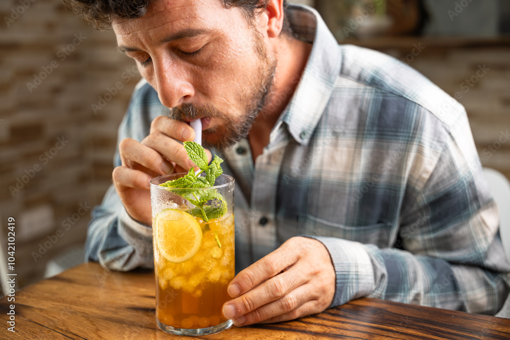 Close-up young man enjoying a piña colada tea cocktail with peach balls, orange or lemon slice and mint, non-alcoholic cocktail, refreshing and healthy drink, free background to write, copy space Close-up young man enjoying a piña colada tea cocktail with peach balls, orange or lemon slice and mint, non-alcoholic cocktail, refreshing and healthy drink, free background to write, copy space
