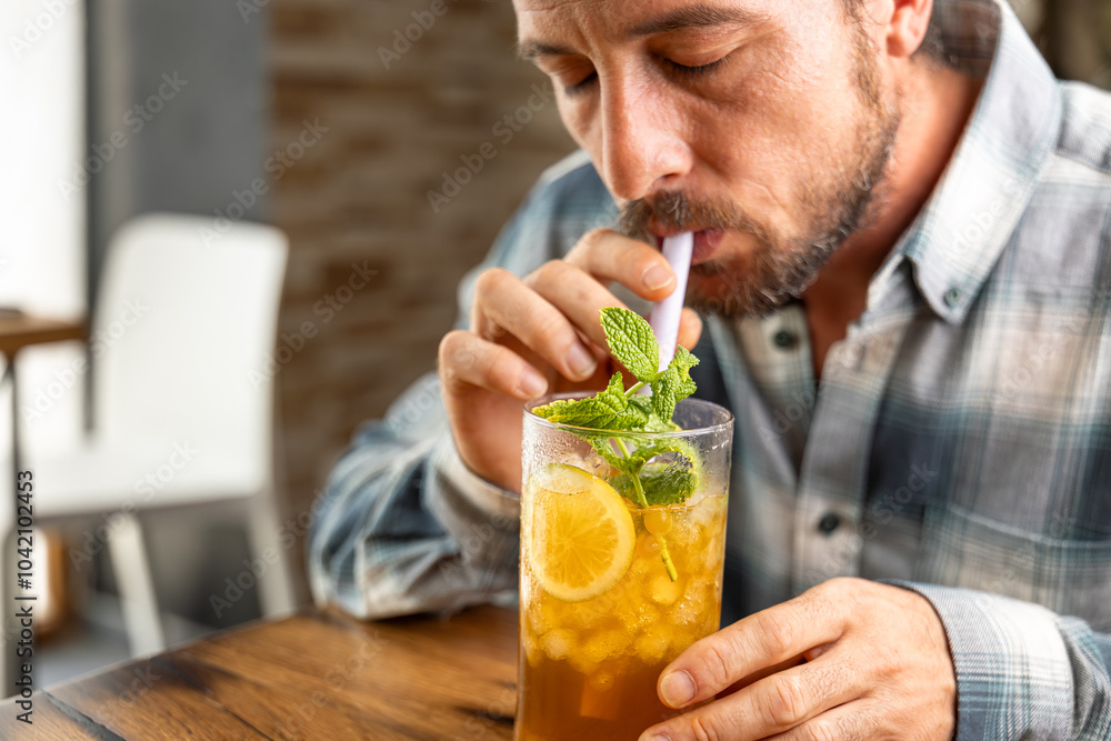 Close-up young man enjoying a piña colada tea cocktail with peach balls, orange or lemon slice and mint, non-alcoholic cocktail, refreshing and healthy drink, free background to write, copy space Close-up young man enjoying a piña colada tea cocktail with peach balls, orange or lemon slice and mint, non-alcoholic cocktail, refreshing and healthy drink, free background to write, copy space