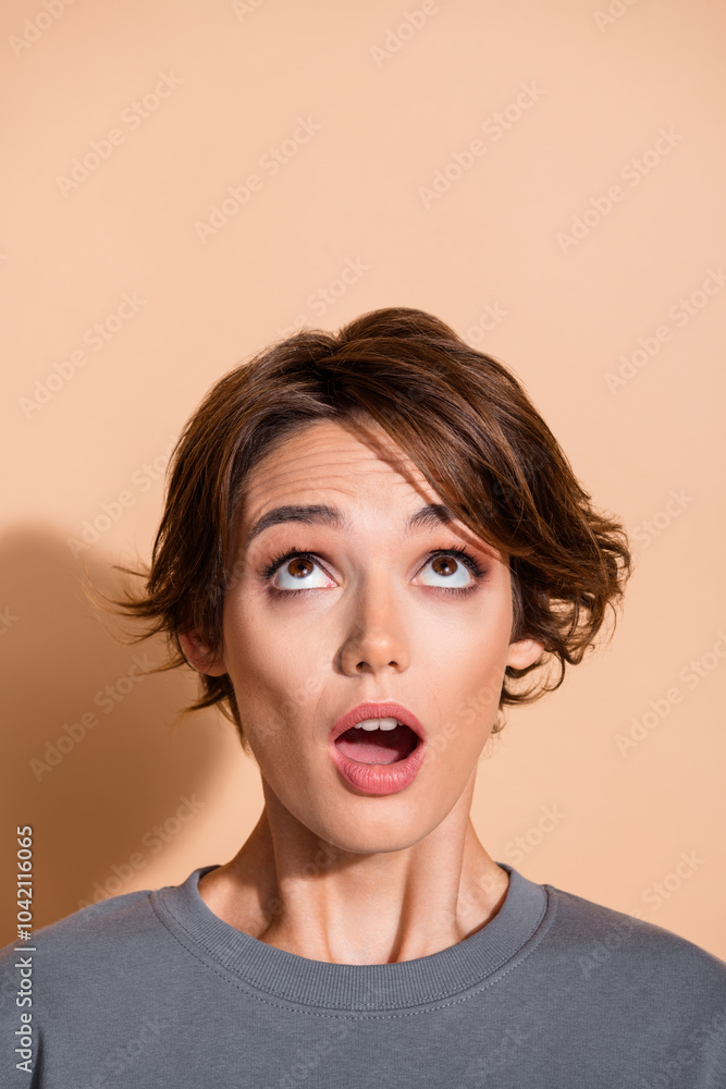 Vertical photo portrait of lovely young lady look up empty space frightened wear trendy gray garment isolated on beige color background Vertical photo portrait of lovely young lady look up empty space frightened wear trendy gray garment isolated on beige color background