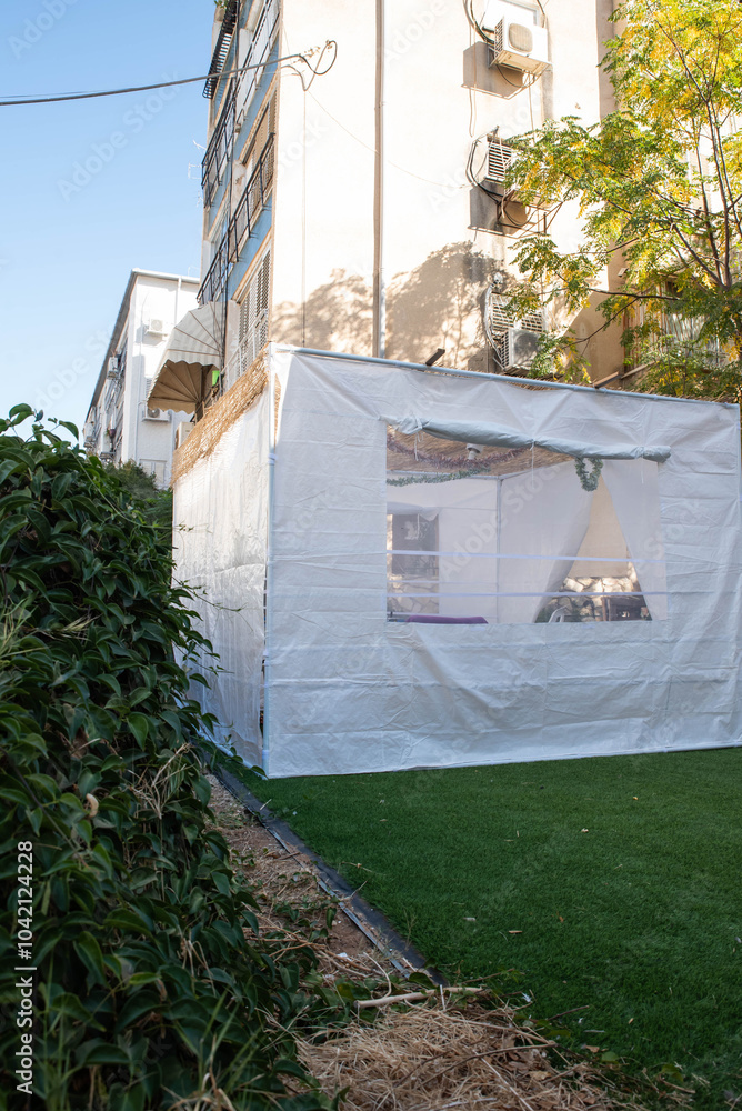 Jewish festival of Sukkot in Israel. Traditional sukkah with handmade decorations near the building on the street. Jewish festival of Sukkot in Israel. Traditional sukkah with handmade decorations near the building on the street.