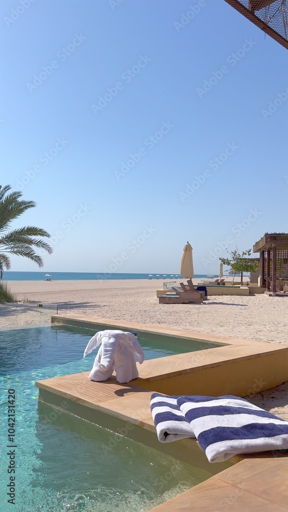 Obraz premium Indulge in luxury hotels resort swimming pool with plus towels and serene sunbathing areas. Nestled by beach and sea, this tourist resort highlights lifestyle of wellbeing and relaxation.