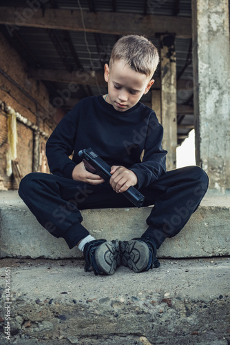 A boy in black clothes sits with a pistol in his hands.